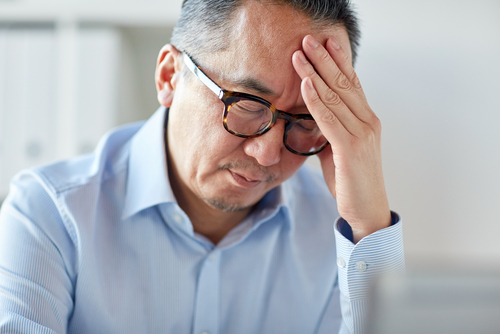Middle-aged man with glasses looking tired and holding head