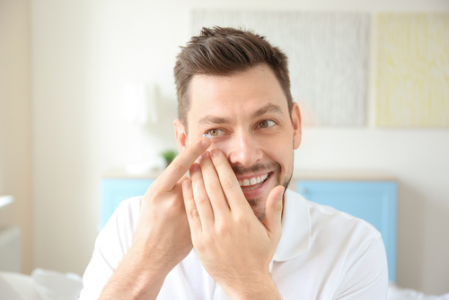 Smiling young man inserting contact lens