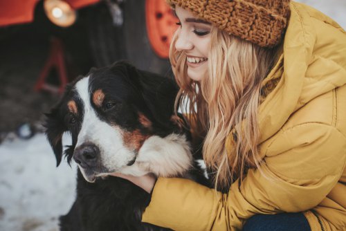 Smiling young woman in winter clothes petting a large dog