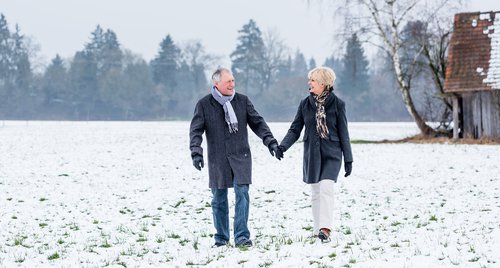 Happy older couple holding hands and walking through a snowy field