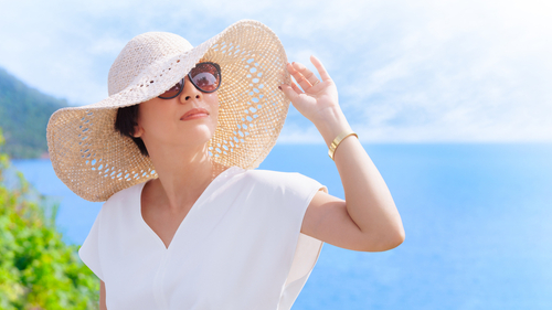 woman in white hat and sunglasses standing in front of the ocean